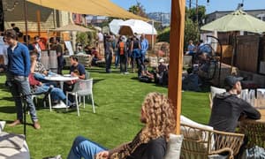 Conference attendees talking in the Lighthaven garden beneath shade sails and a timber pergola in Berkeley